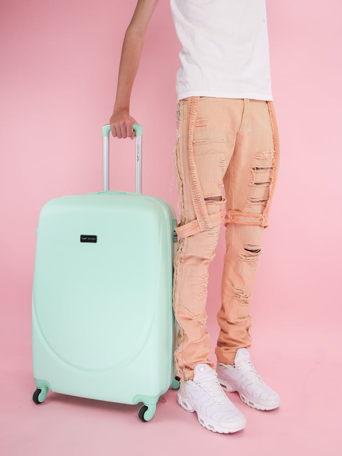 Fashionable young adult with a mint suitcase against a pink background.