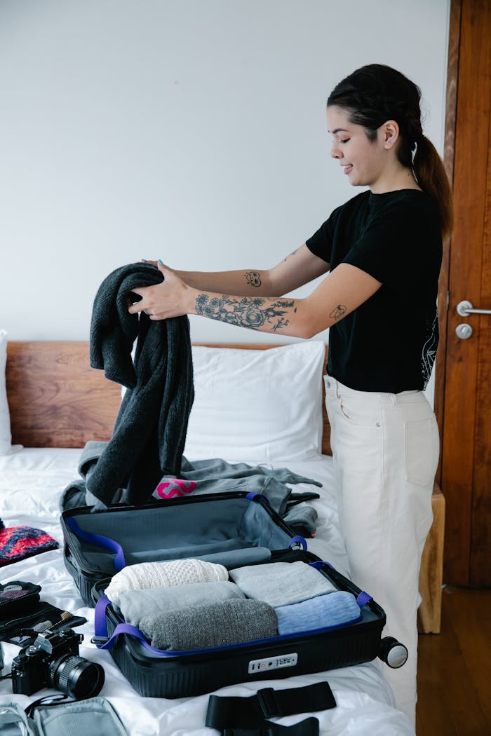 A woman with tattoos packs her clothes into luggage, preparing for a trip.